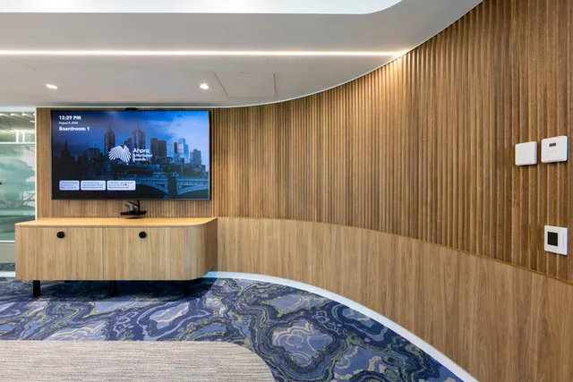 A curved fluted timber wall in a boardroom, with a timber credenza with rounded ends and round black pulls on black legs below a wall-mounted screen.